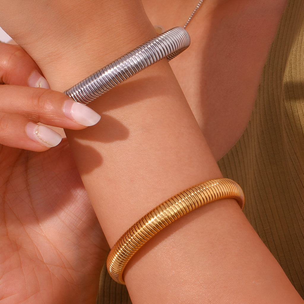 Bracelet jonc flexible en maille acier inoxydable or porté au poignet avec un bracelet argenté tenu à la main.