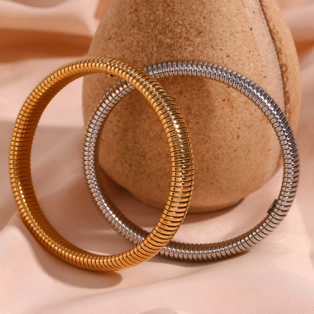 Bracelet jonc flexible en maille acier inoxydable couleur or et argent posé sur support beige.