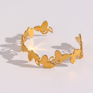 Bracelet jonc doré en acier inoxydable avec motifs floraux et papillons ajourés.