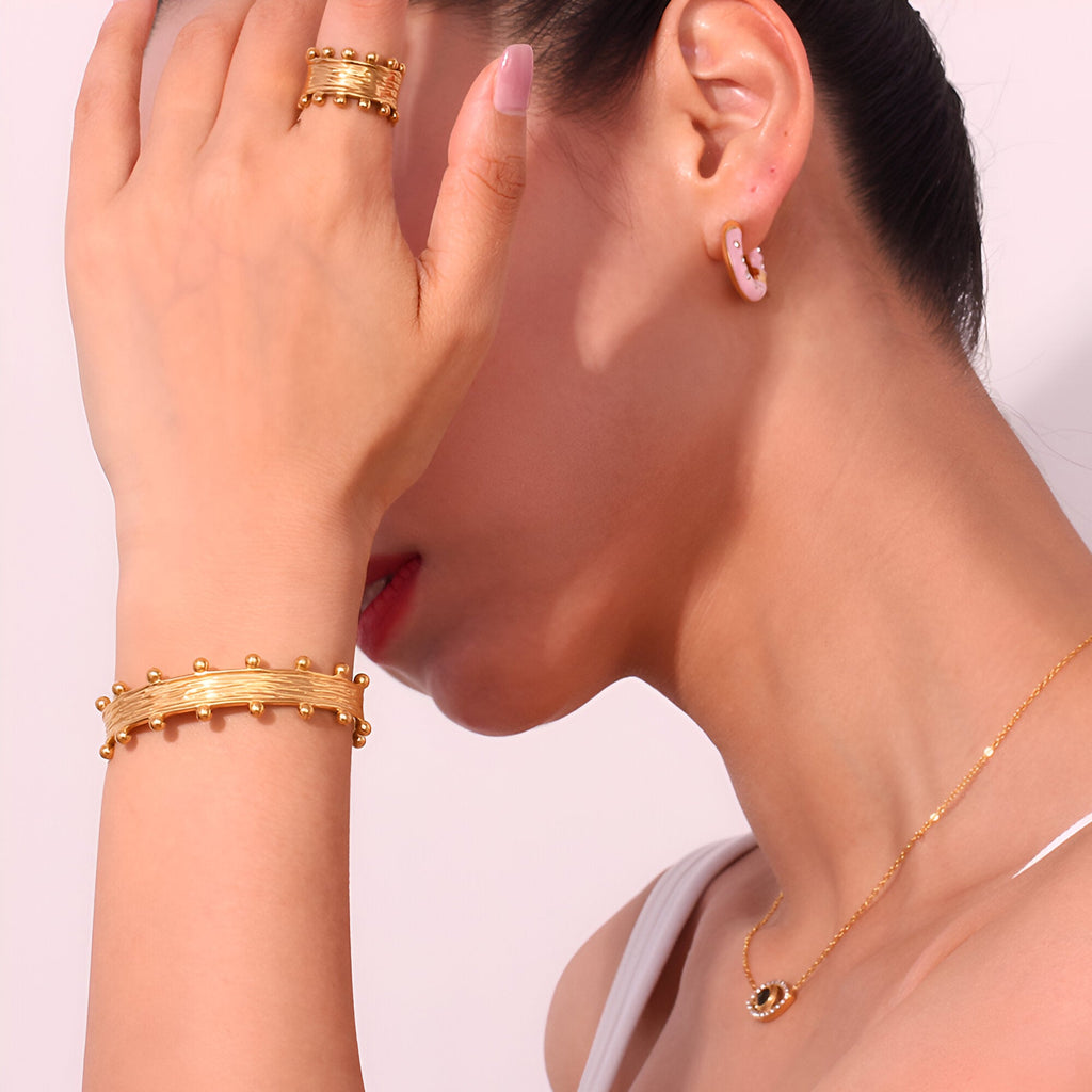 Bracelet jonc doré 18 carats avec motifs sphériques, porté au poignet féminin élégant.