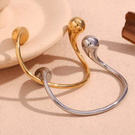Bracelet jonc en acier inoxydable or et argent avec extrémités sphériques lisses et design minimaliste.