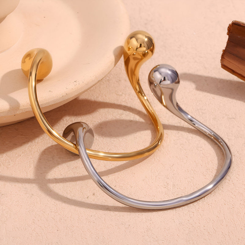 Bracelet jonc en acier inoxydable or et argent avec extrémités sphériques lisses et design minimaliste.