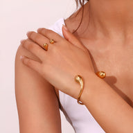 Bracelet jonc doré en acier inoxydable avec design fluide et boules aux extrémités porté au poignet.