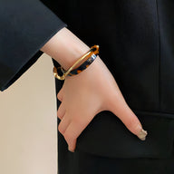 Bracelet jonc léopard en acrylique effet écaille et métal doré porté au poignet féminin élégamment habillé.