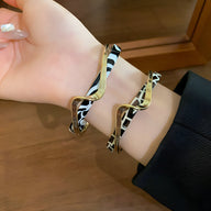 Bracelet jonc léopard en acrylique noir et blanc avec détail métal doré, modèle Valencia, porté au poignet.