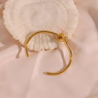 Bracelet jonc fin en acier inoxydable doré avec nœud infini élégant posé sur tissu rose pâle.