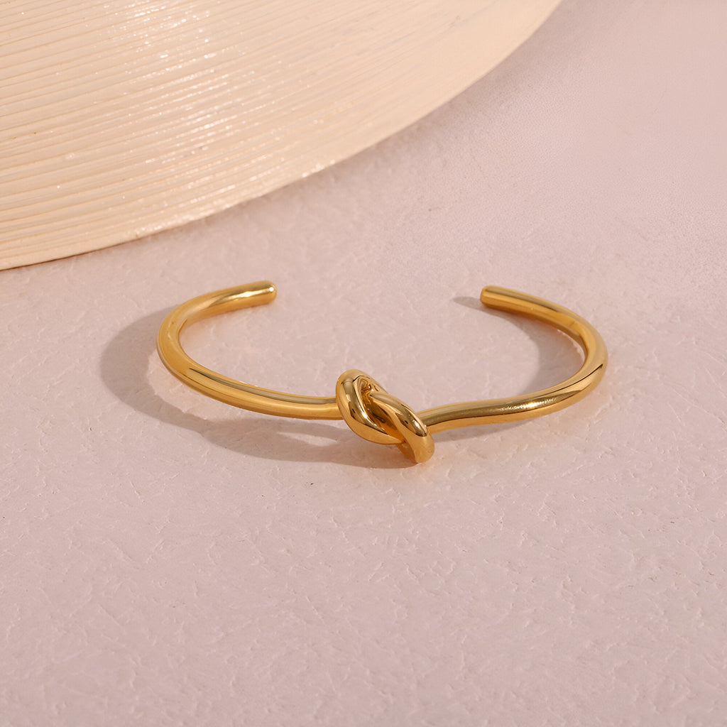 Bracelet jonc en acier inoxydable doré avec nœud central style Infini, finition brillante.