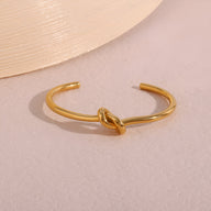 Bracelet jonc en acier inoxydable doré avec nœud central style Infini, finition brillante.