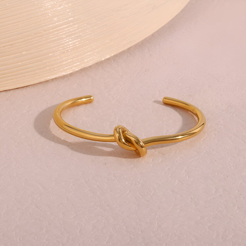 Bracelet jonc en acier inoxydable doré avec nœud central style Infini, finition brillante.