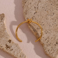 Bracelet jonc or en acier inoxydable avec nœud infini élégant sur fond pierre beige.