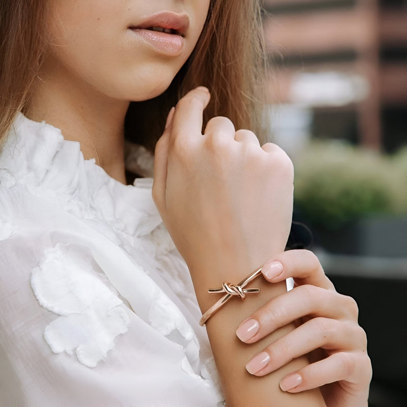 Bracelet jonc or avec nœud délicat en acier inoxydable porté au poignet féminin.
