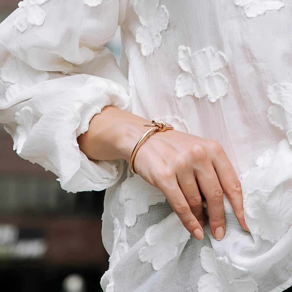 Bracelet jonc en acier inoxydable or rosé avec nœud délicat porté sur poignet féminin.