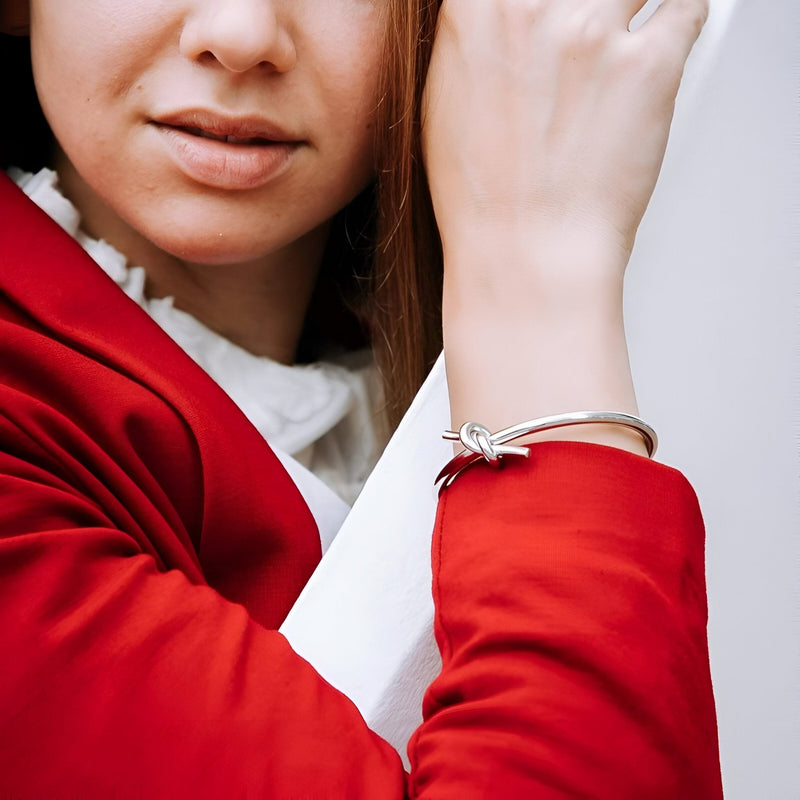Bracelet jonc argenté en acier inoxydable avec nœud délicat porté sur poignet féminin.