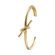 Bracelet jonc fin en acier inoxydable doré avec nœud décoratif central.