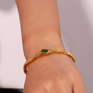 Bracelet jonc ondulé en acier doré avec pierre verte rectangulaire élégante.