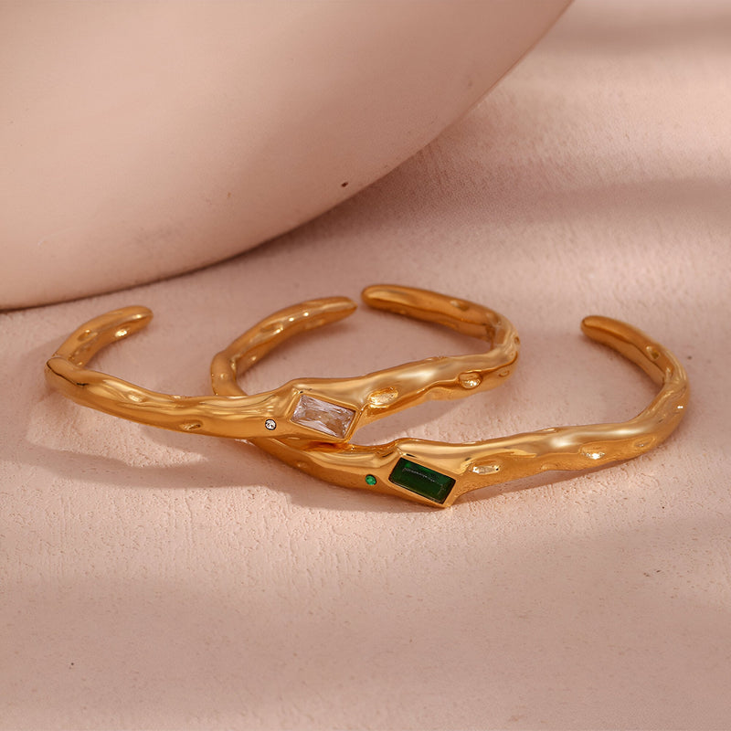 Bracelet jonc ondulé en acier inoxydable doré avec pierres rectangulaires blanche et verte.