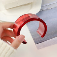 Bracelet jonc ouvert en résine rouge translucide à effet marbré, finition lisse et brillante.