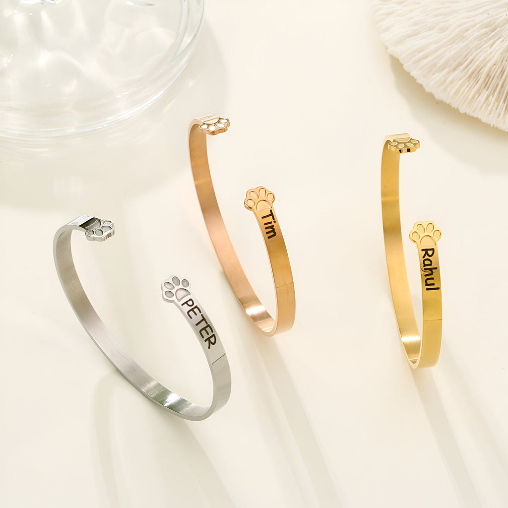 Trois bracelets joncs personnalisés en argent, or rosé et or avec patte d'animal gravée et noms différents.