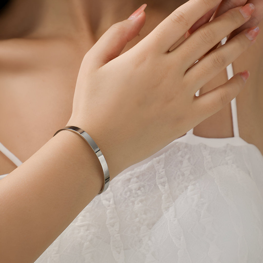 Bracelet jonc fin en argent avec motif patte d'animal porté sur poignet féminin en robe blanche délicate.