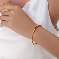 Bracelet jonc fin en acier inoxydable doré, design épuré, porté au poignet féminin.