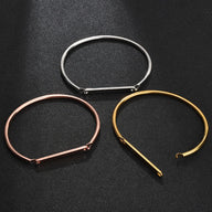 Trois bracelets joncs en acier inoxydable personnalisés aux finis or, argent et or rosé sur fond noir.