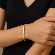 Bracelet jonc fin en acier inoxydable doré avec plaque personnalisable porté au poignet femme.