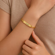 Bracelet jonc en acier inoxydable doré personnalisé avec gravure "Louise" porté au poignet féminin.