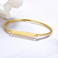 Bracelet jonc en acier inoxydable doré avec plaque personnalisable lisse et fermoir minimaliste.