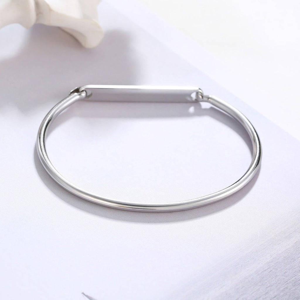 Bracelet jonc fin en acier inoxydable argenté avec plaque personnalisable lisse et fermoir discret.