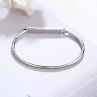 Bracelet jonc fin en acier inoxydable argenté avec plaque personnalisable lisse et fermoir discret.