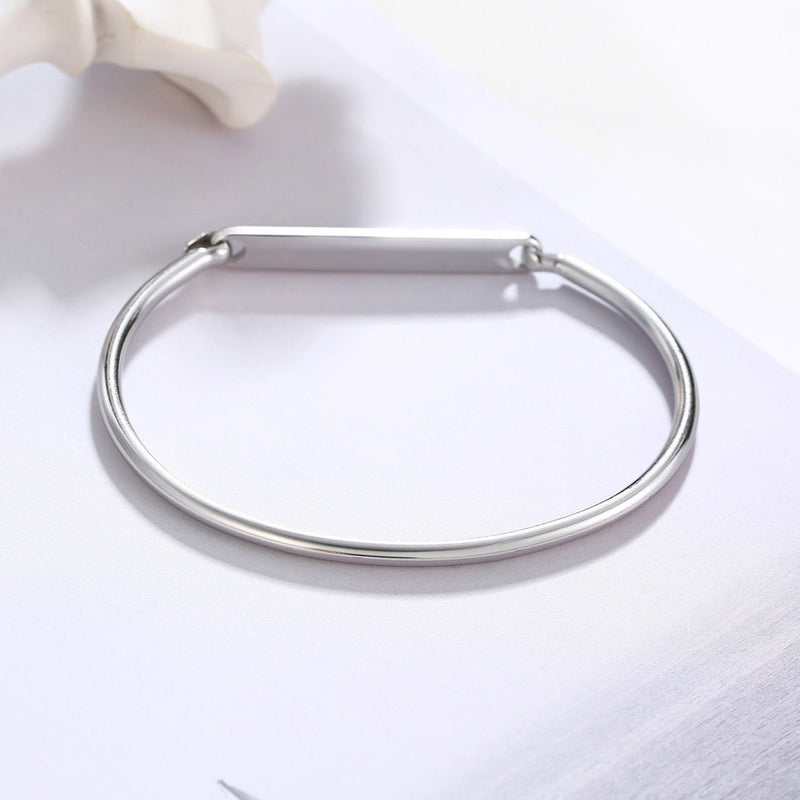 Bracelet jonc fin en acier inoxydable argenté avec plaque personnalisable lisse et fermoir discret.