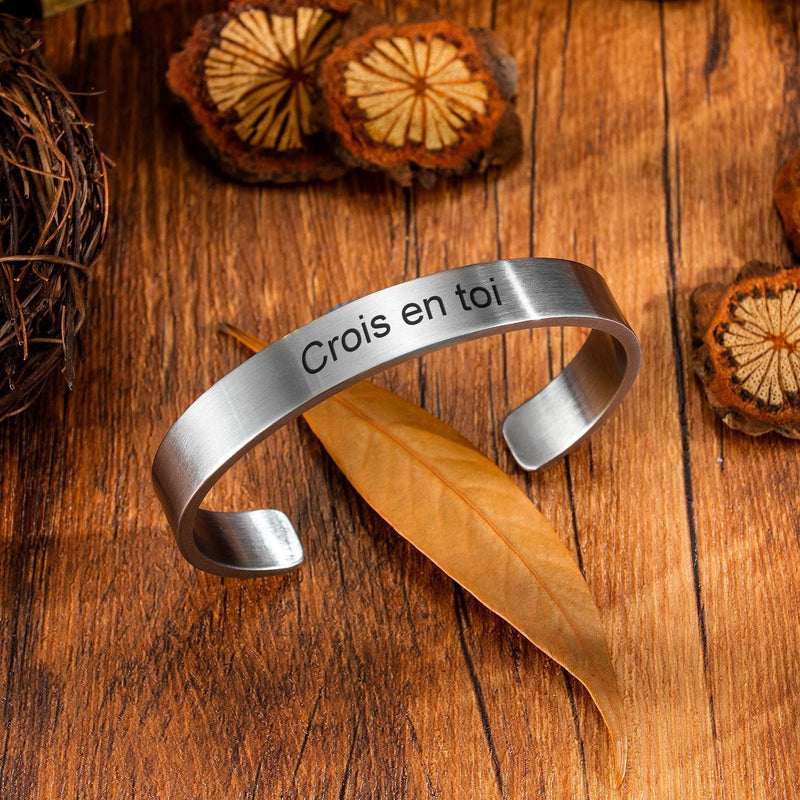 Bracelet jonc homme en acier inoxydable argenté avec gravure "Crois en toi" sur fond en bois.