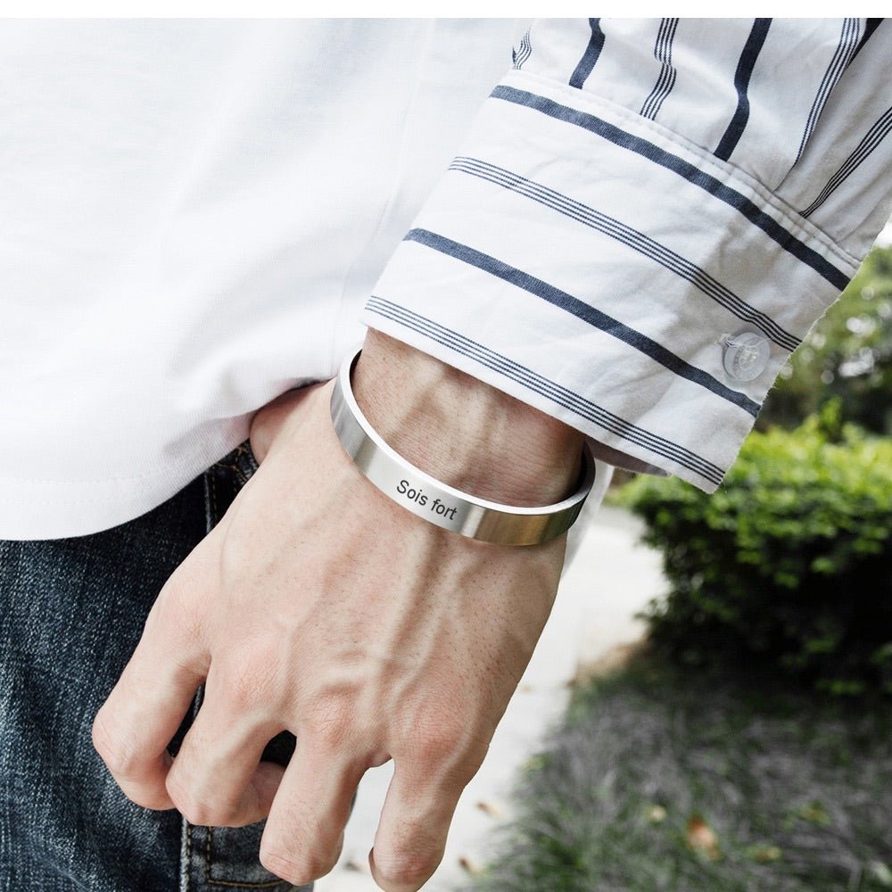 Bracelet jonc en acier inoxydable argenté avec gravure personnalisée, porté au poignet d’un homme, style épuré et moderne.