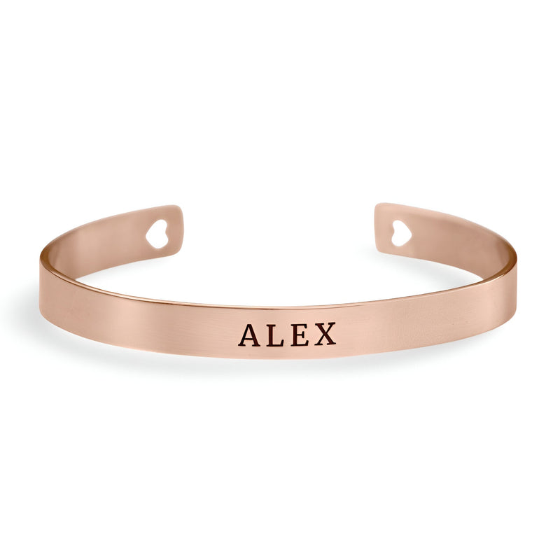 Bracelet jonc en or rosé avec gravure personnalisée "ALEX" et découpes cœur aux extrémités.