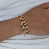 Bracelet jonc fin en acier doré avec petites pierres colorées, style minimaliste pour femme.