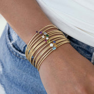 Bracelet jonc fin en acier doré avec pierre de naissance colorée, modèle Adéni, porté au poignet.
