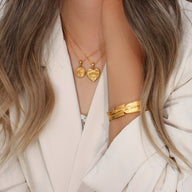 Bracelet jonc or en acier inoxydable avec motif plume délicat porté au poignet féminin.