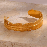 Bracelet jonc doré en acier inoxydable en forme de plume avec détails texturés délicats.