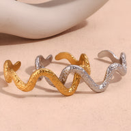 Bracelet jonc serpentin en acier inoxydable doré et argenté avec texture martelée.