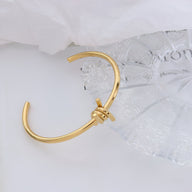 Bracelet jonc fin en titane plaqué or 18 carats avec détail noué élégant.