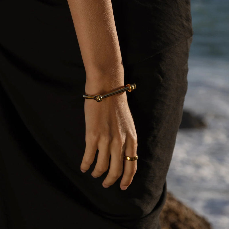 Bracelet jonc titane or au crochet d'ancrage porté avec une bague assortie sur fond noir.