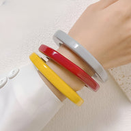 Bracelets joncs irréguliers en résine aux couleurs jaune, rouge et gris clair portés sur le poignet.