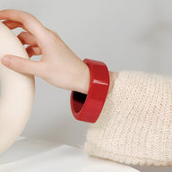 Bracelet jonc large en résine rouge cerise porté sur poignet féminin avec pull en maille crème.