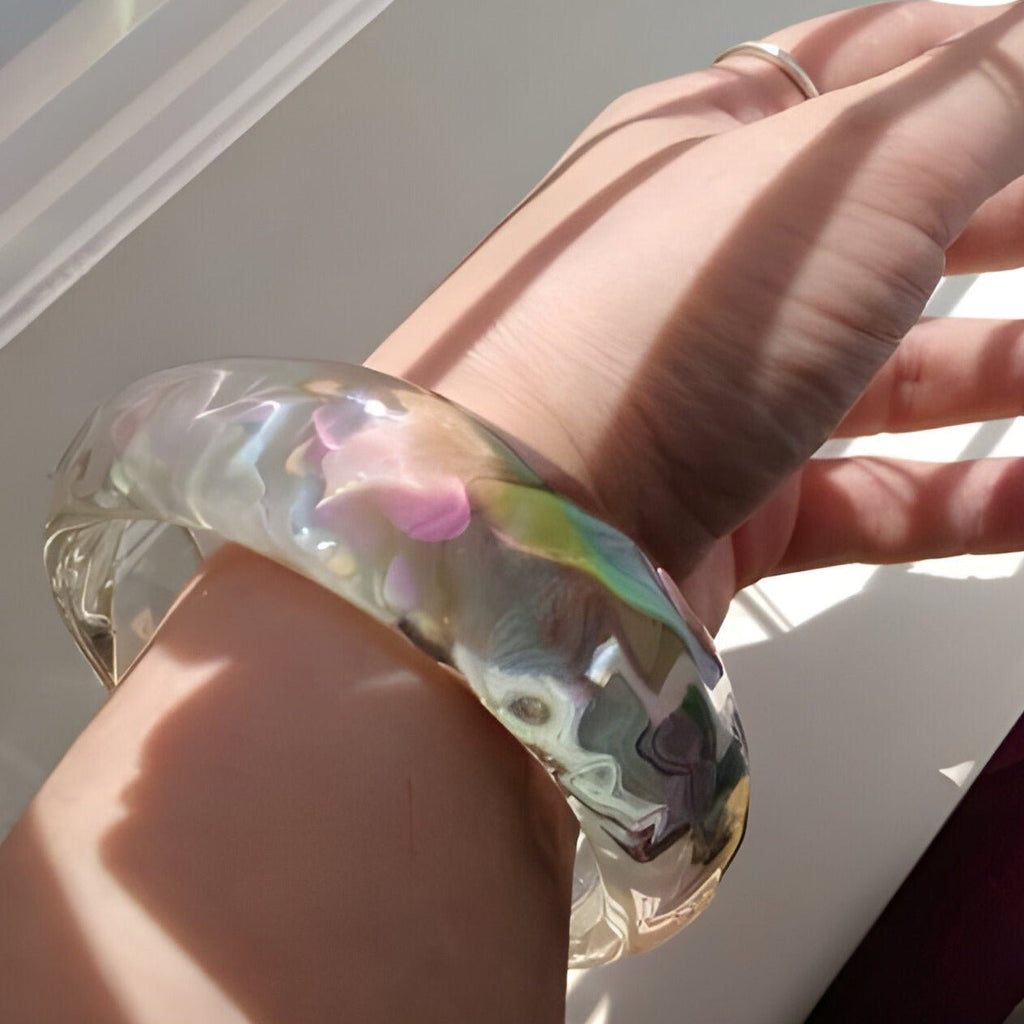 Bracelet jonc en résine transparente aux reflets irisés multicolores, style lumineux, porté au poignet féminin.