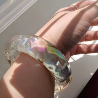 Bracelet jonc en résine transparente aux reflets irisés multicolores, style lumineux, porté au poignet féminin.