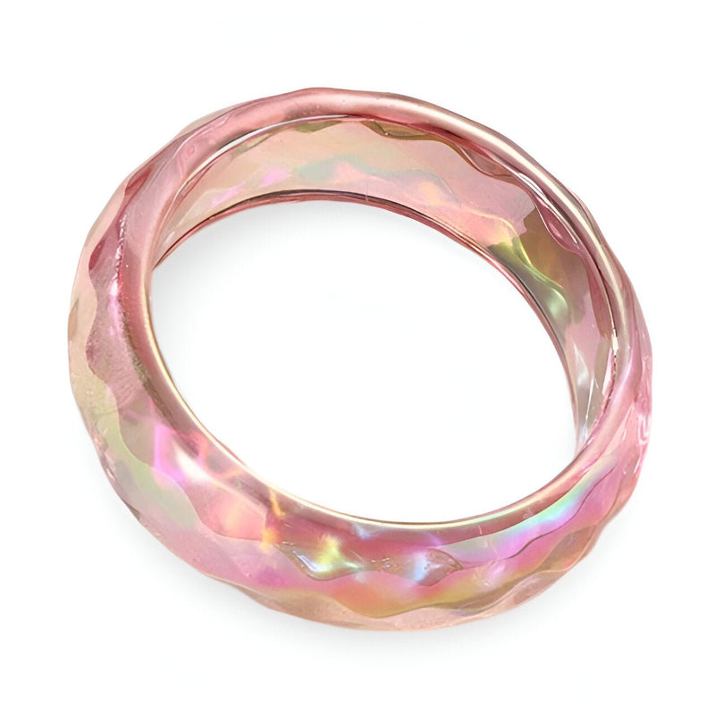 Bracelet jonc en résine translucide rose aux reflets lumineux et surface facettée.