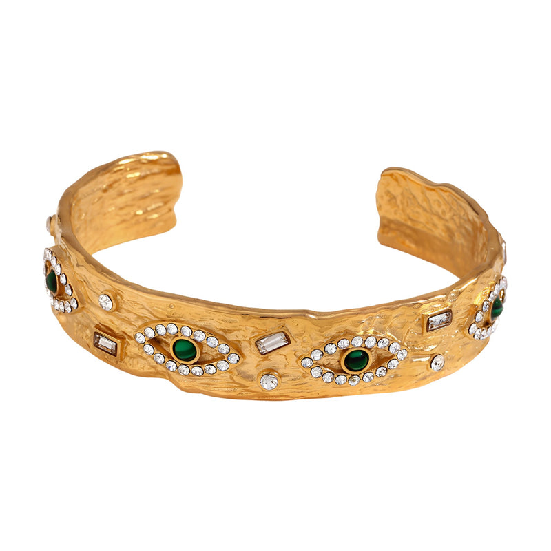 Bracelet jonc doré texturé orné d'yeux verts et de petits cristaux brillants.