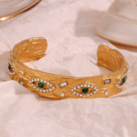 Bracelet jonc en acier inoxydable doré avec motifs d'yeux verts et strass blancs scintillants.