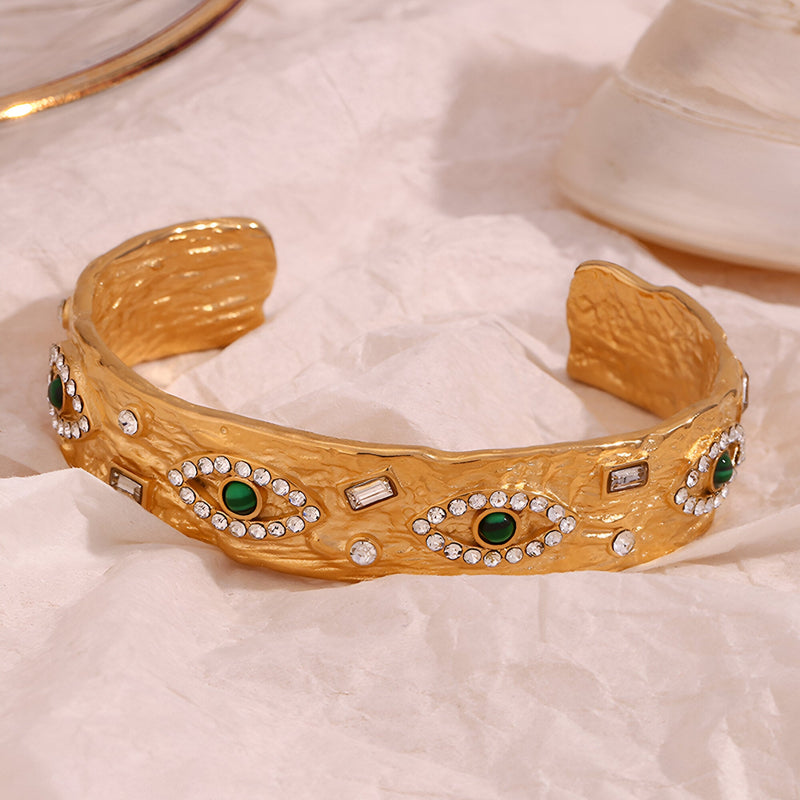 Bracelet jonc en acier inoxydable doré avec motifs d'yeux verts et strass blancs scintillants.