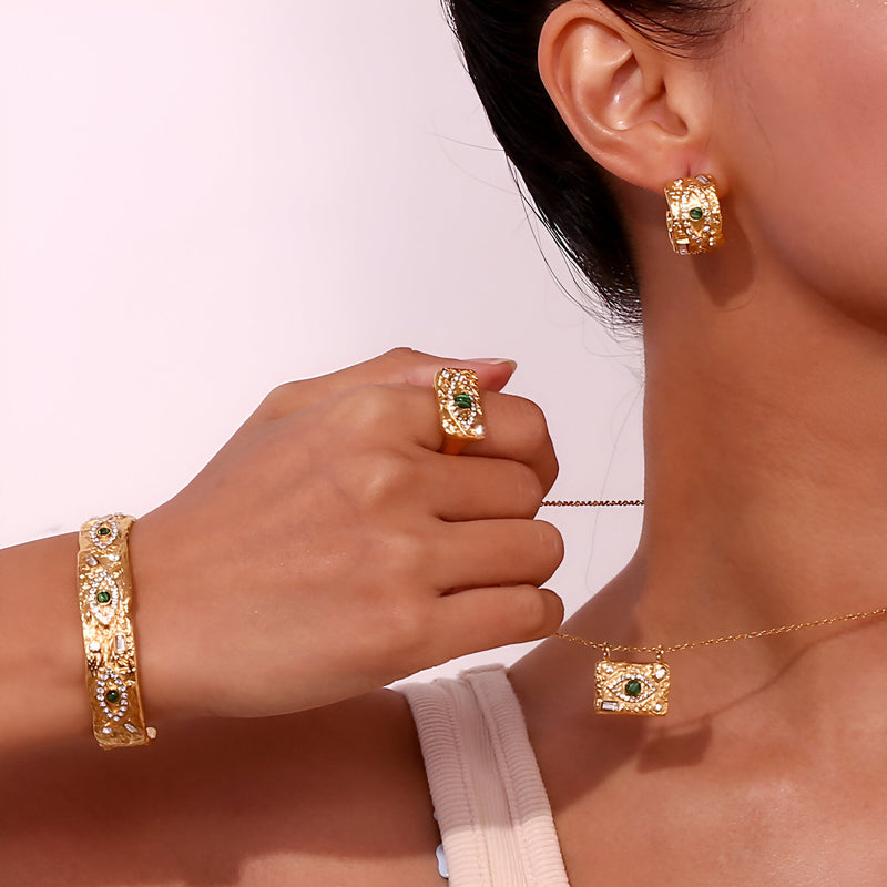 Bracelet jonc en acier inoxydable doré avec motif œil vert, bague et boucle d’oreille assorties.